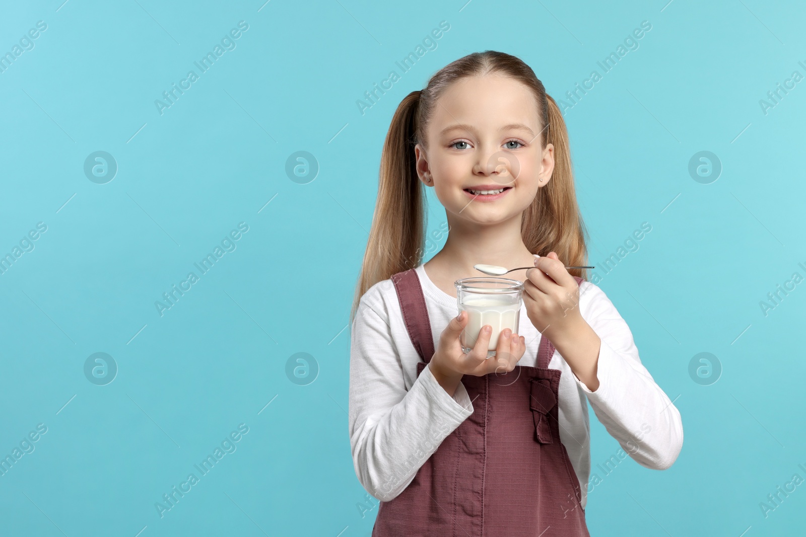 Photo of Cute little girl with tasty yogurt on light blue background, space for text