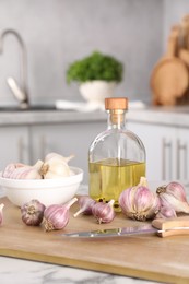 Photo of Fresh raw garlic, knife and oil on white marble table, closeup