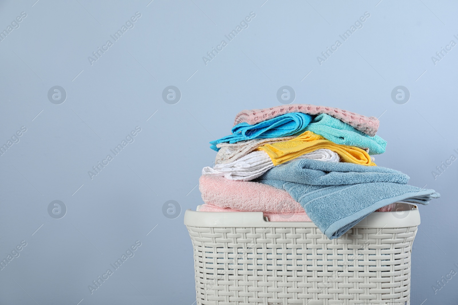 Photo of Laundry basket with clean towels on color background. Space for text