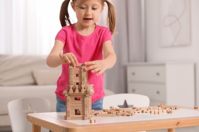 Cute little girl playing with wooden tower at table indoors. Child's toy