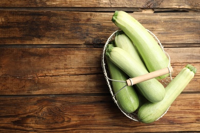Photo of Basket with ripe zucchinis on wooden table, top view. Space for text