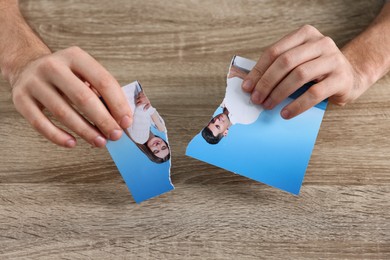 Photo of Man holding parts of photo at table indoors, closeup. Divorce concept