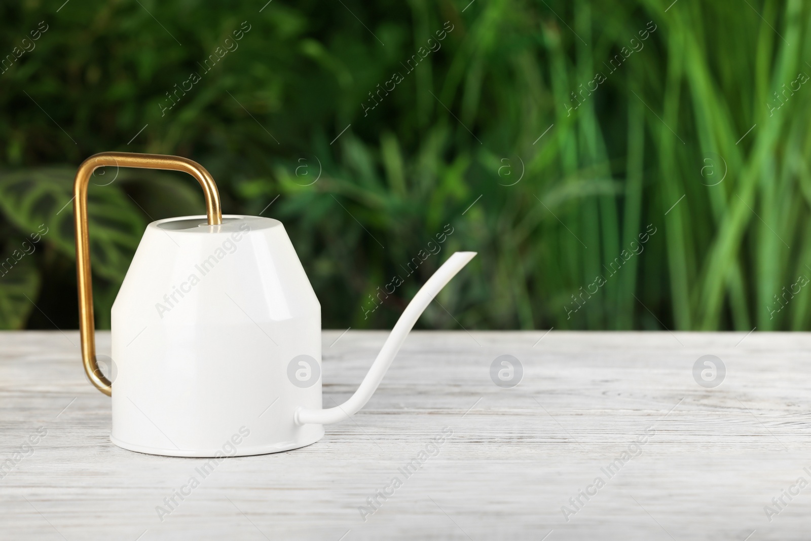 Photo of Stylish watering can on white wooden table against blurred background. Space for text
