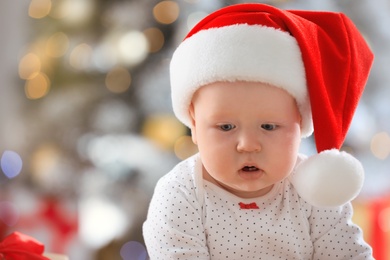Photo of Little baby wearing Santa hat indoors. First Christmas