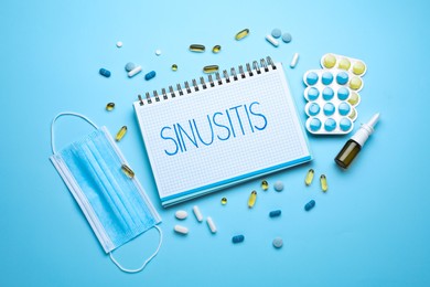 Photo of Notebook with word SINUSITIS, medical mask and different drugs on light blue background, flat lay
