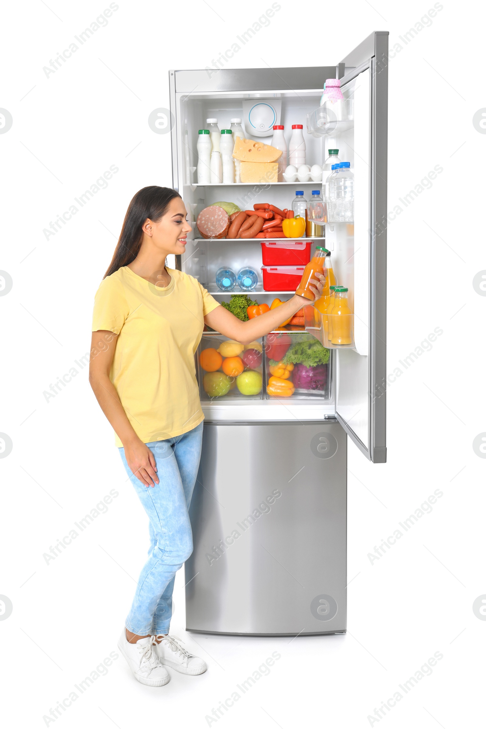 Photo of Young woman taking bottle of juice from refrigerator on white background