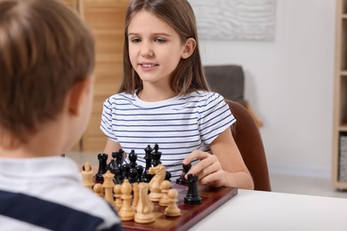 Cute children playing chess at table in room