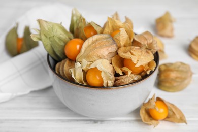 Ripe physalis fruits with dry husk on white wooden table, closeup