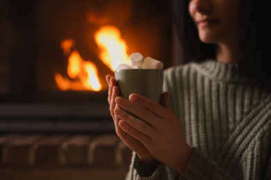 Woman with cup of sweet cocoa near fireplace indoors, closeup