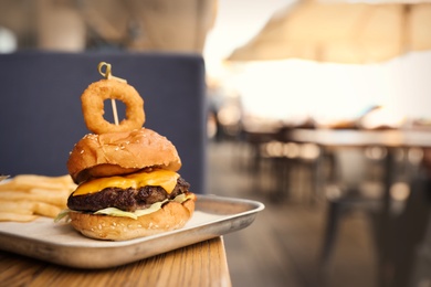 Photo of Delicious burger with onion ring on table in street cafe. Space for text