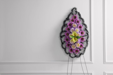 Funeral wreath of plastic flowers near white wall, space for text