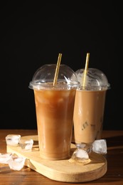 Photo of Refreshing iced coffee with milk in takeaway cups on wooden table against black background