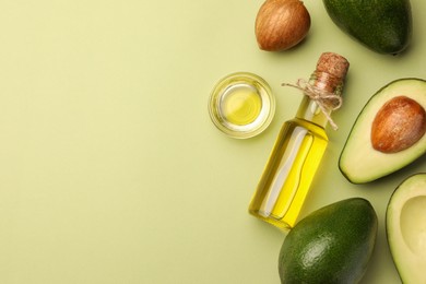 Photo of Cooking oil and fresh avocados on light green background, flat lay. Space for text