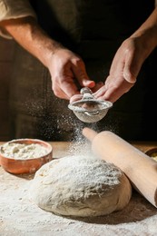 Photo of Man sprinkling flour over dough at wooden table, closeup