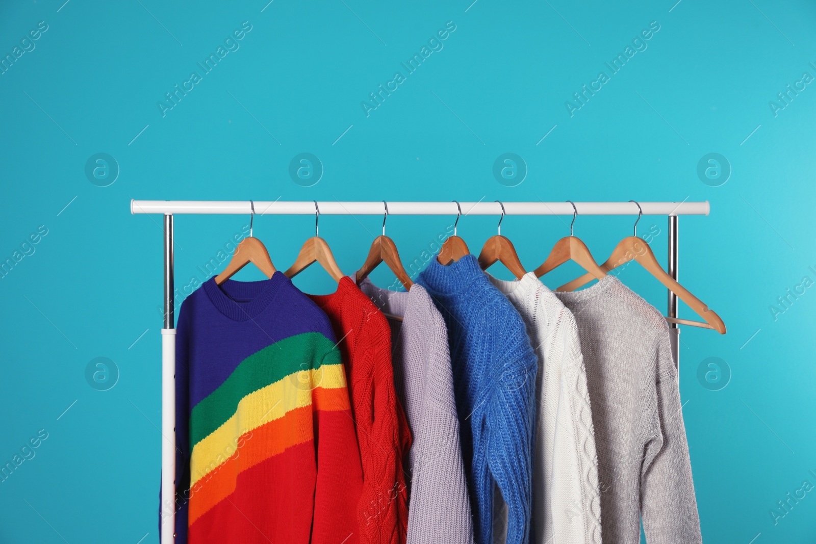 Photo of Collection of warm sweaters hanging on rack against color background