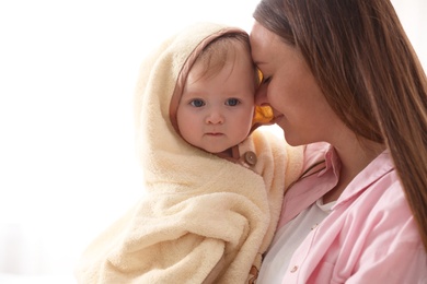 Photo of Mother holding cute little baby wrapped with hooded towel after bath on light background, closeup