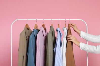 Photo of Woman taking stylish jacket from clothes rack against pink background, closeup