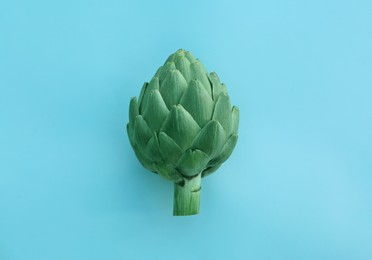 Photo of Whole fresh raw artichoke on light blue background, top view