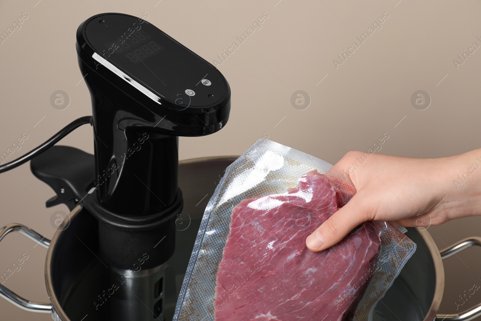 Photo of Woman putting vacuum packed meat into pot with thermal immersion circulator, closeup. Sous vide cooking