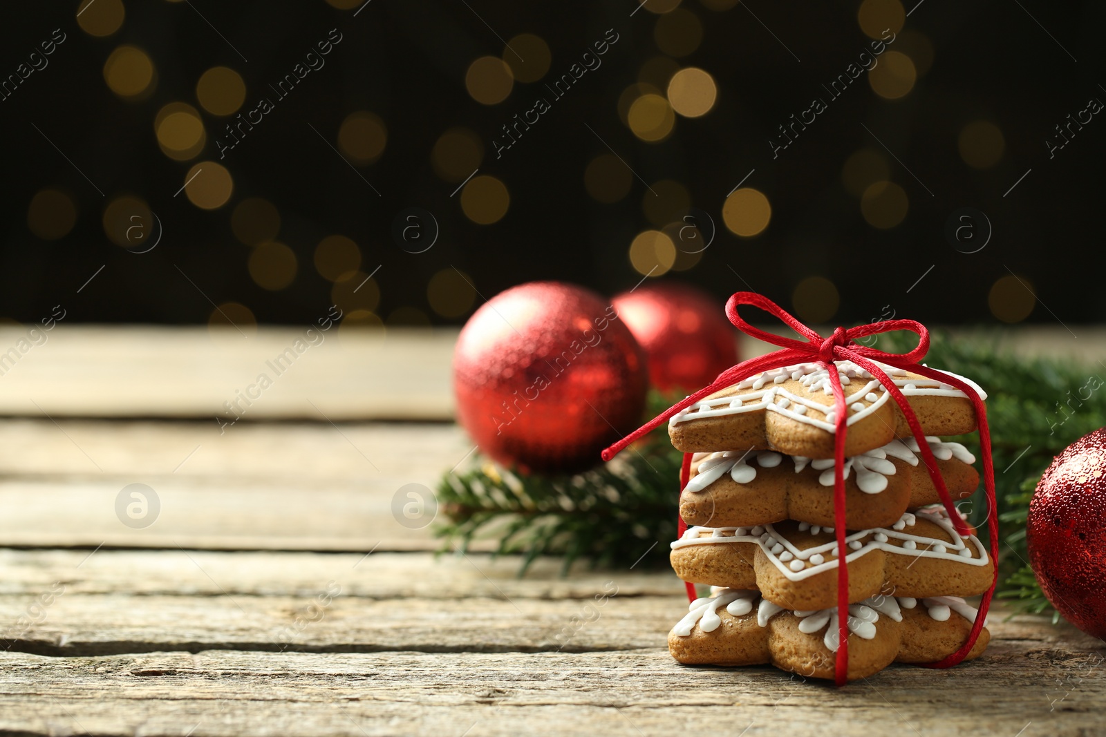 Photo of Tasty Christmas cookies with icing on wooden table against blurred lights. Space for text