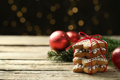 Photo of Tasty Christmas cookies with icing on wooden table against blurred lights. Space for text