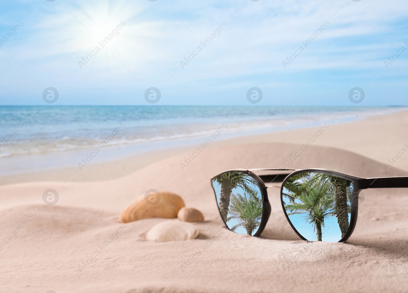 Image of Palms reflecting in sunglasses on sandy beach with seashells near sea