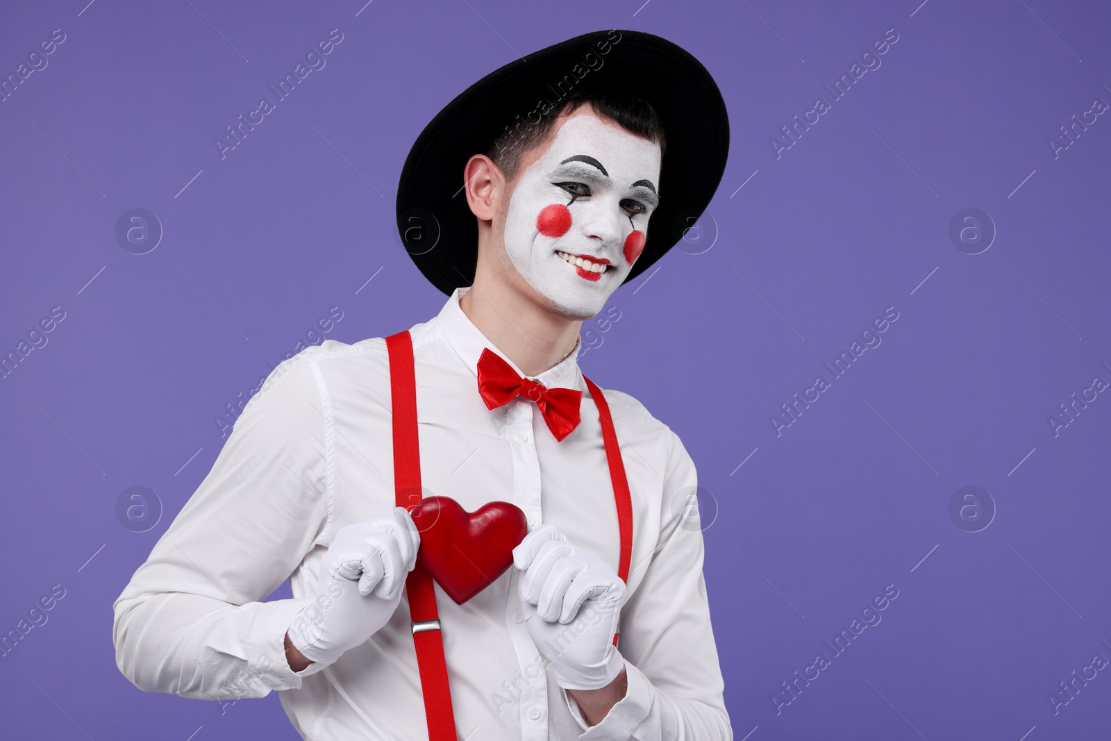 Photo of Funny mime artist with red heart on purple background