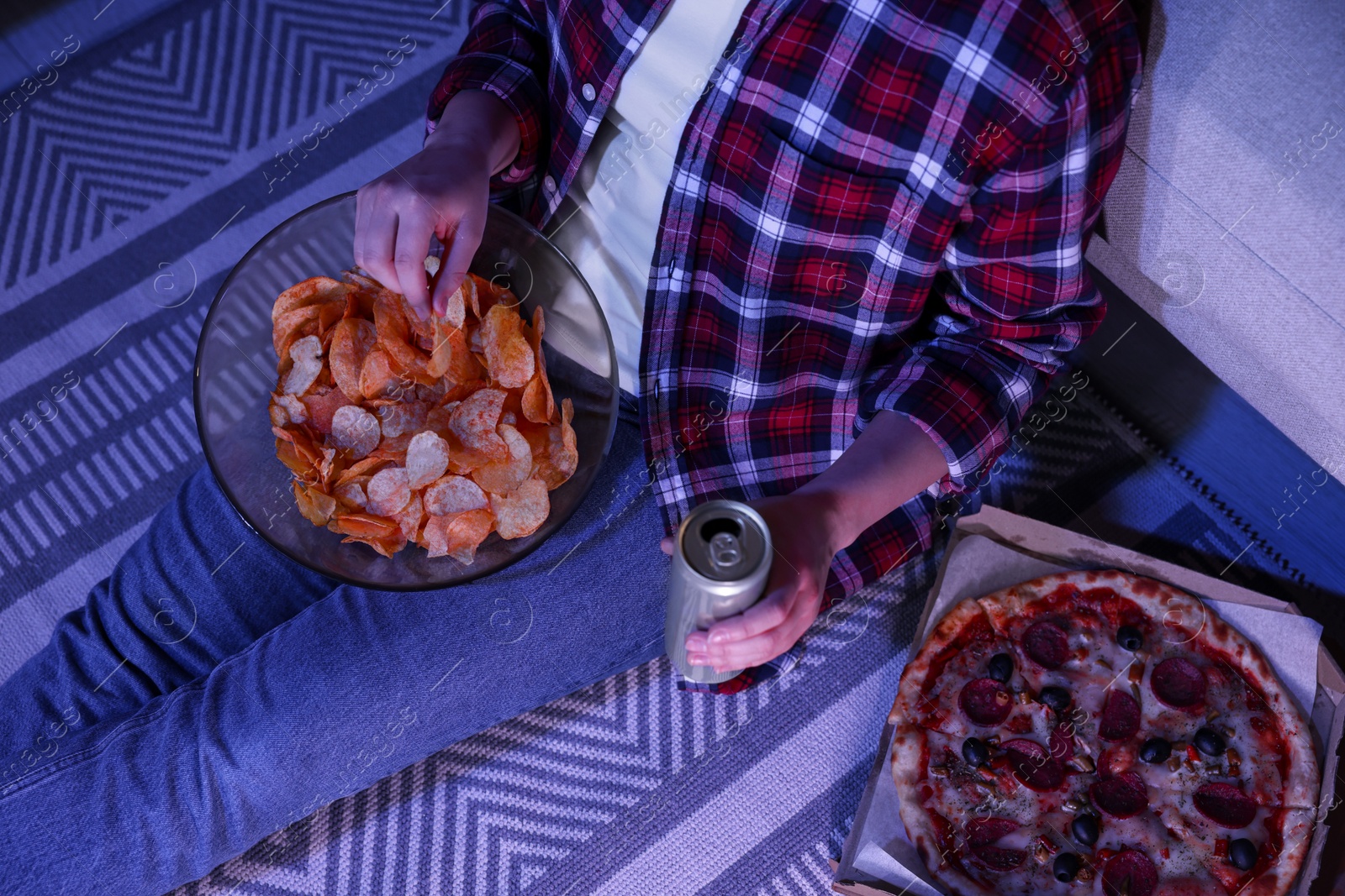 Photo of Young woman with tin can and chips in room at night, closeup. Bad habit