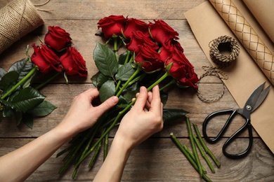Photo of Woman making luxury bouquet of fresh roses at 
 wooden table, top view