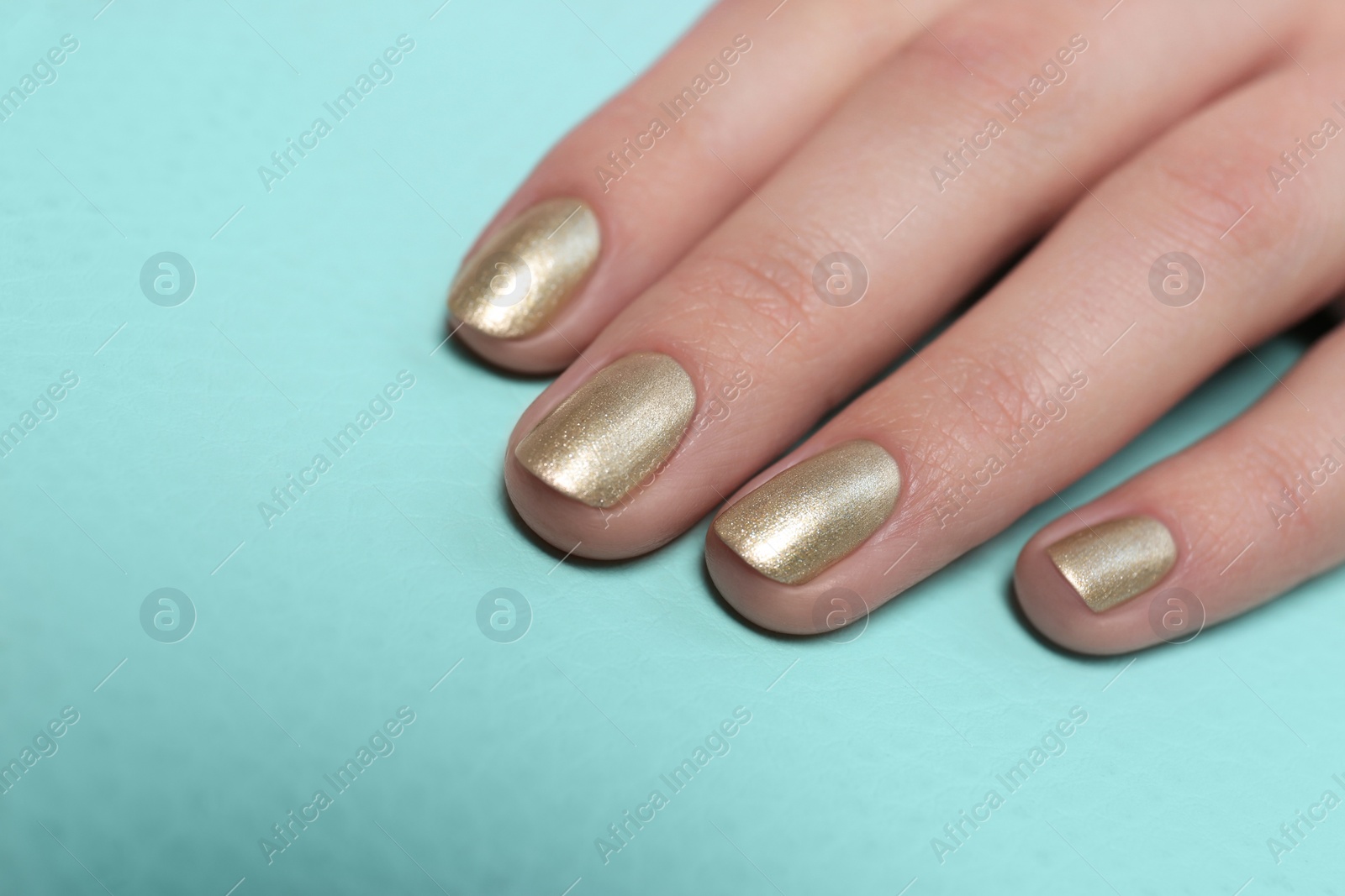 Photo of Woman with golden manicure on color background, closeup. Nail polish trends