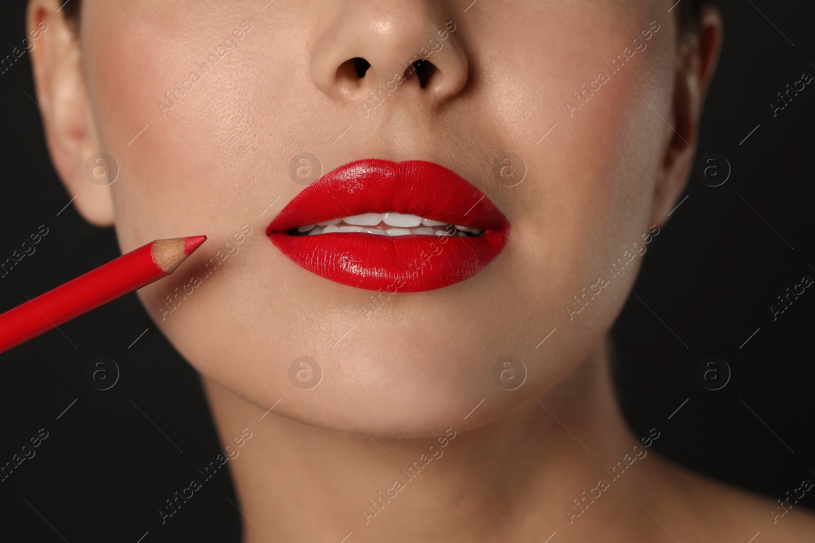 Photo of Young woman with beautiful red lip pencil on black background, closeup