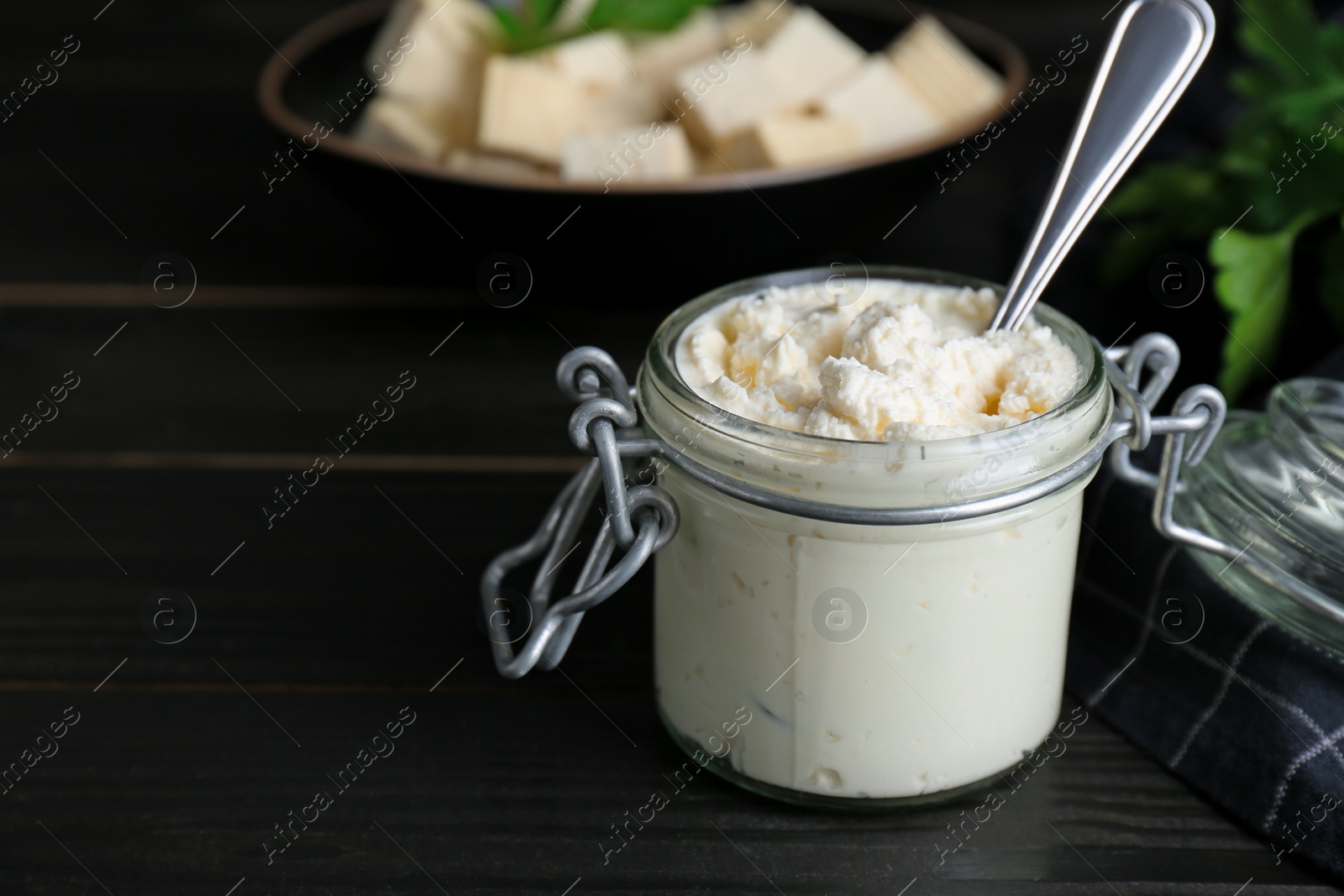 Photo of Delicious tofu cream cheese in glass jar on black wooden table, closeup. Space for text