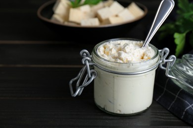 Photo of Delicious tofu cream cheese in glass jar on black wooden table, closeup. Space for text