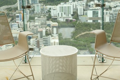 Coffee table and beige chairs against picturesque landscape of city in cafe