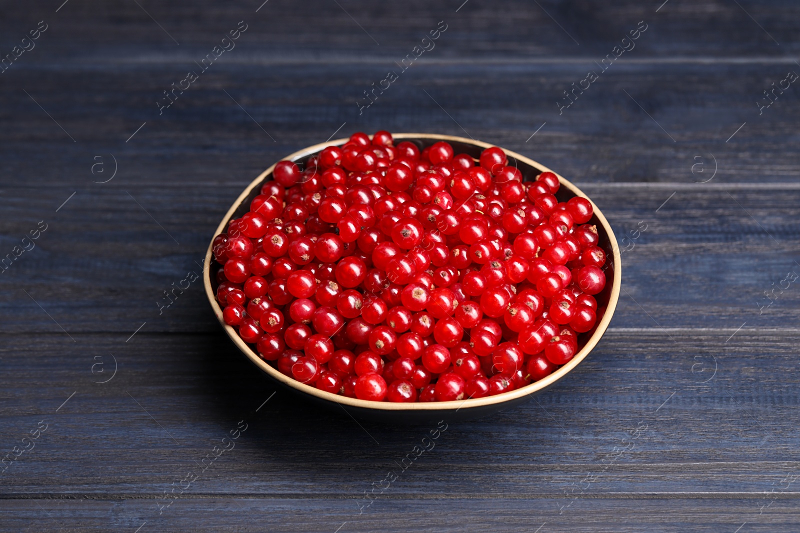 Photo of Ripe red currants in bowl on wooden rustic table