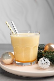 Glass of delicious eggnog and decorated fir branch on gray table
