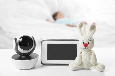 Photo of Baby monitor, camera and toy on table near bed with child in room. Video nanny