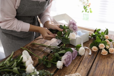 Florist making beautiful wedding bouquet at wooden table, closeup