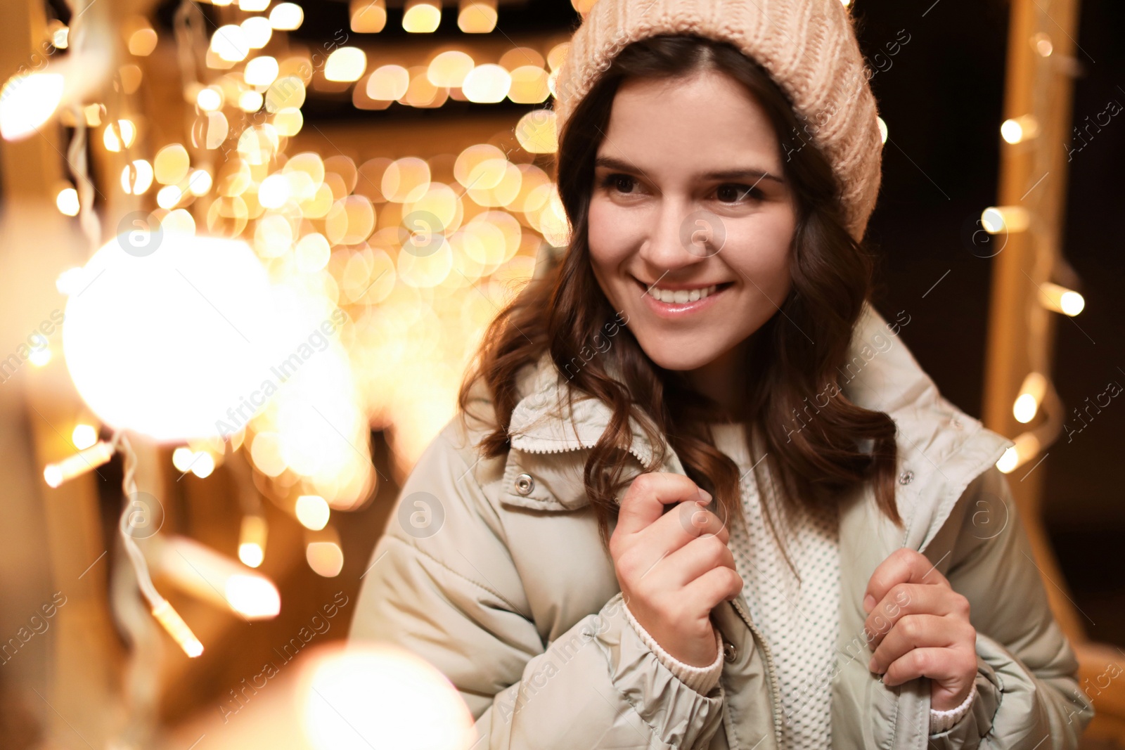 Photo of Beautiful young woman near festive lights outdoors. Winter vacation