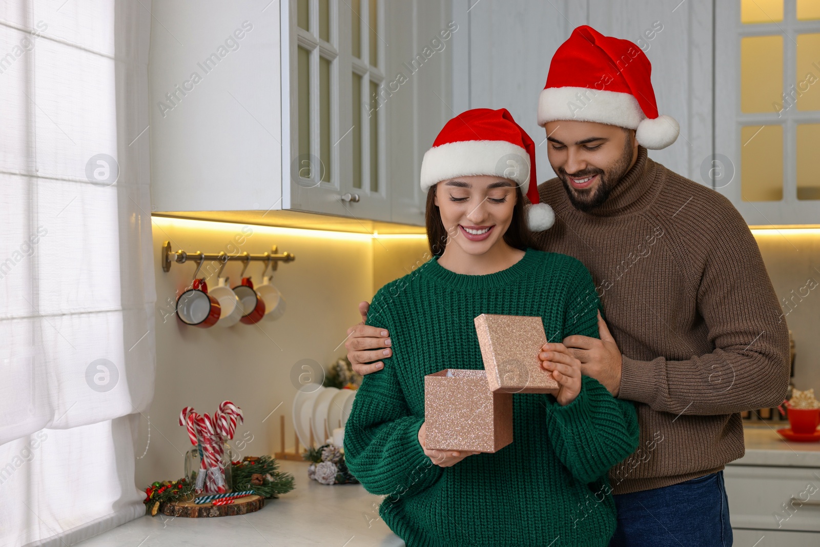 Photo of Beautiful young woman in Santa hat opening Christmas gift from her boyfriend at home