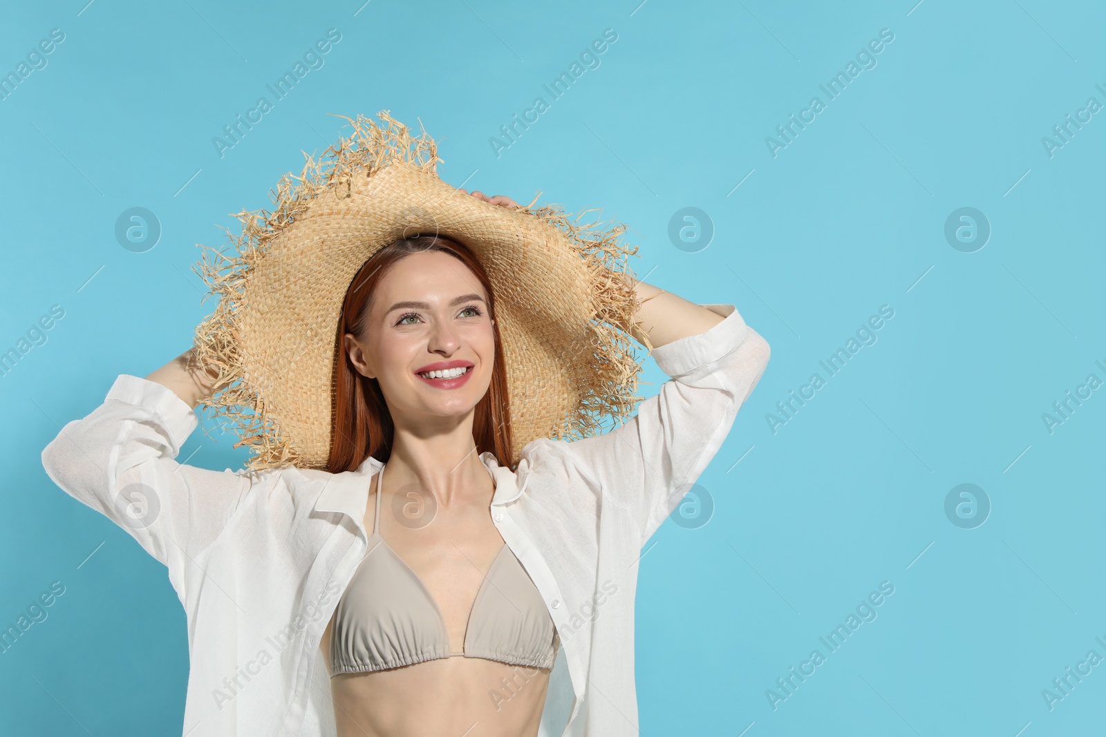 Photo of Beautiful young woman in straw hat on light blue background, space for text