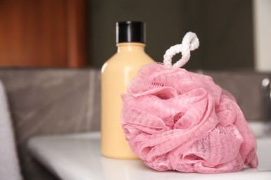 Pink sponge and shower gel bottle on washbasin in bathroom, closeup. Space for text