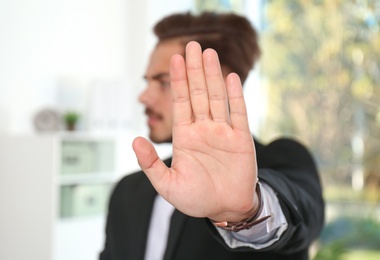 Photo of Man showing stop gesture in office. Problem of sexual harassment at work