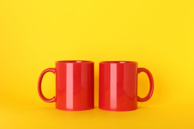 Photo of Blank red ceramic mugs on yellow background
