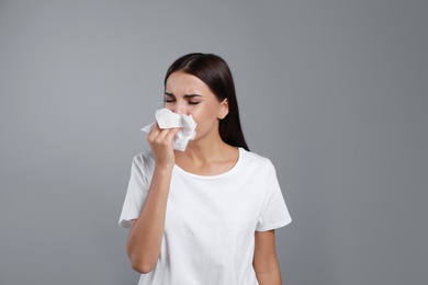 Young woman suffering from allergy on grey background