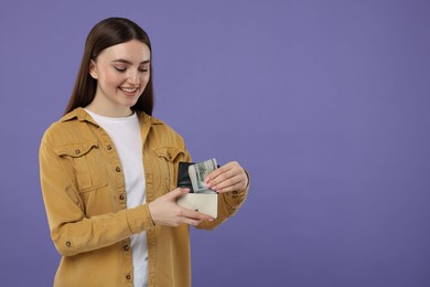 Happy woman putting dollar banknotes into wallet on purple background, space for text