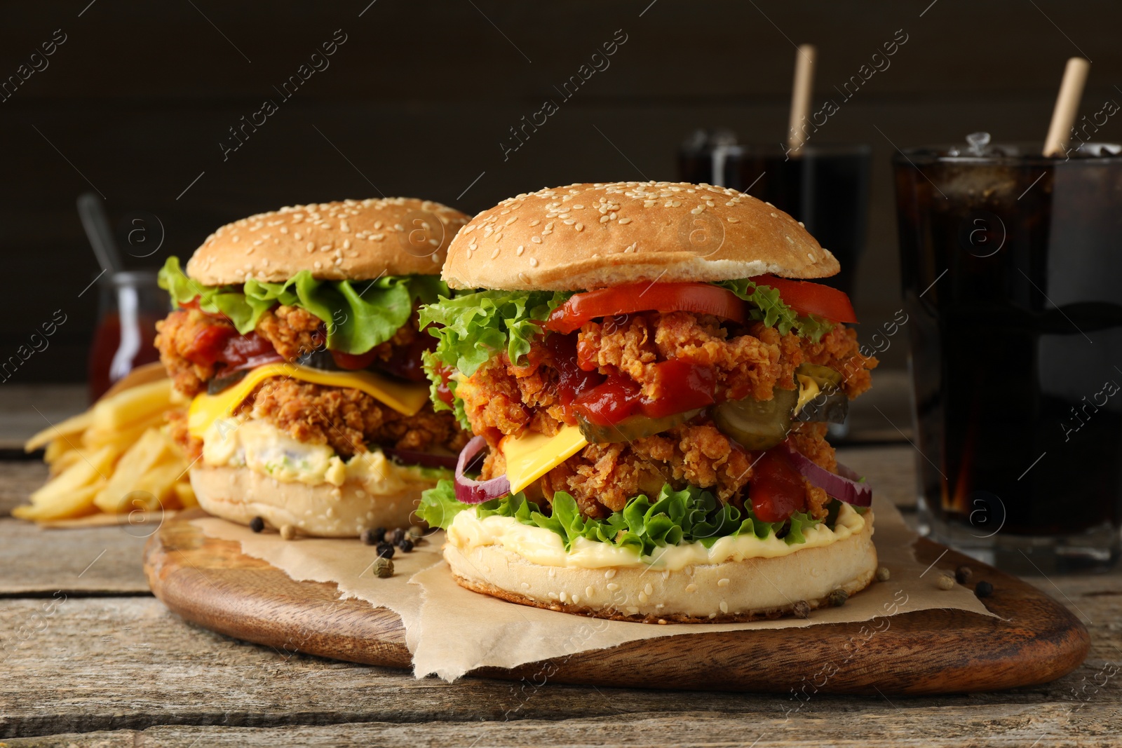 Photo of Delicious burgers with crispy chicken patty, french fries and soda drinks on wooden table