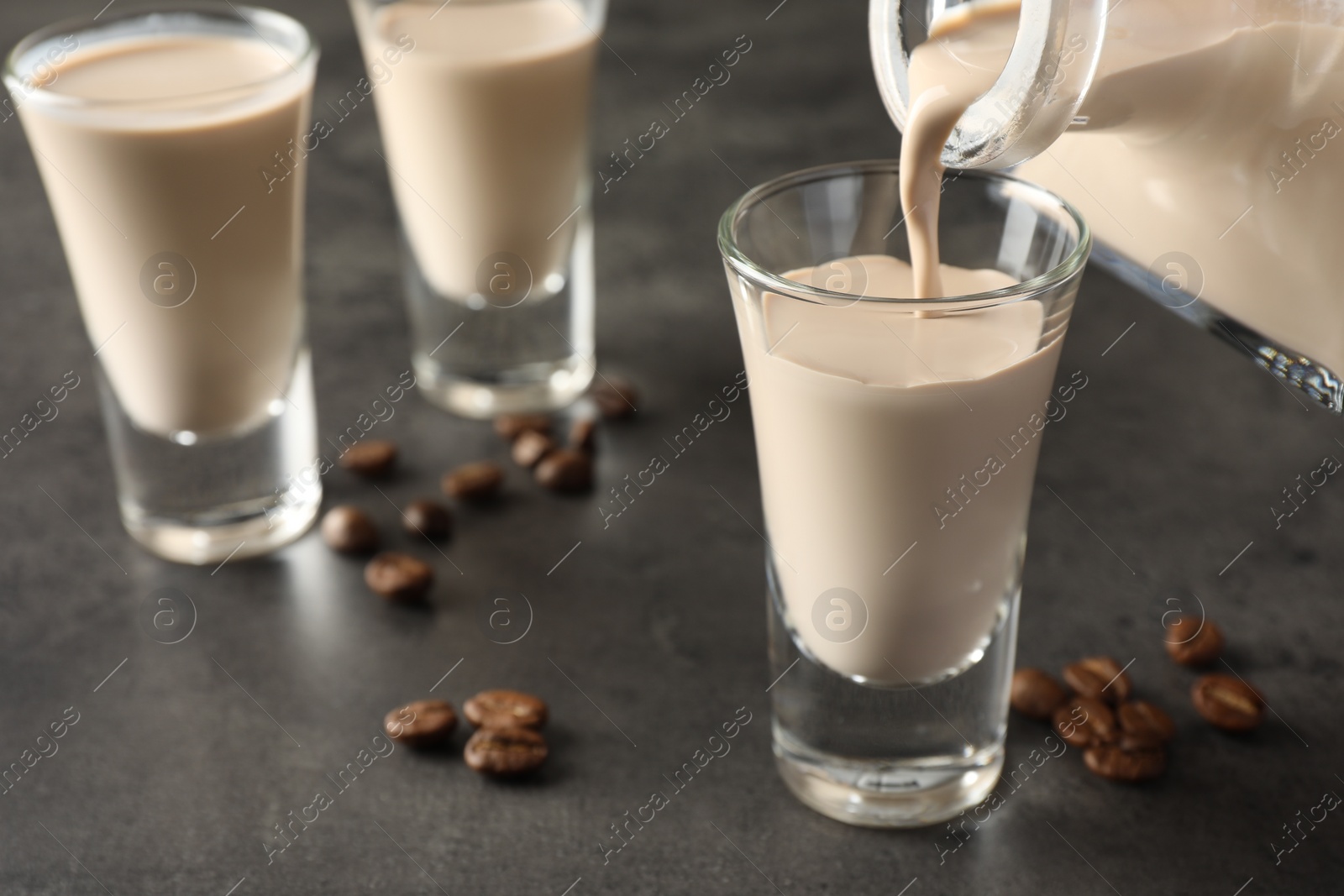 Photo of Pouring coffee cream liqueur into glass at grey table, closeup