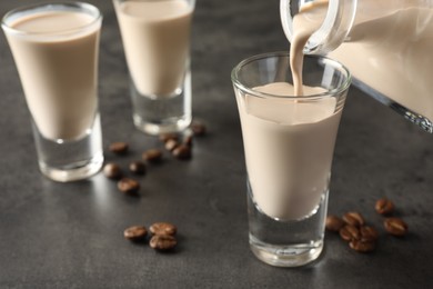 Pouring coffee cream liqueur into glass at grey table, closeup