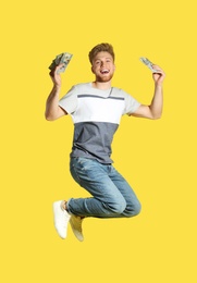 Young man jumping with money on color background
